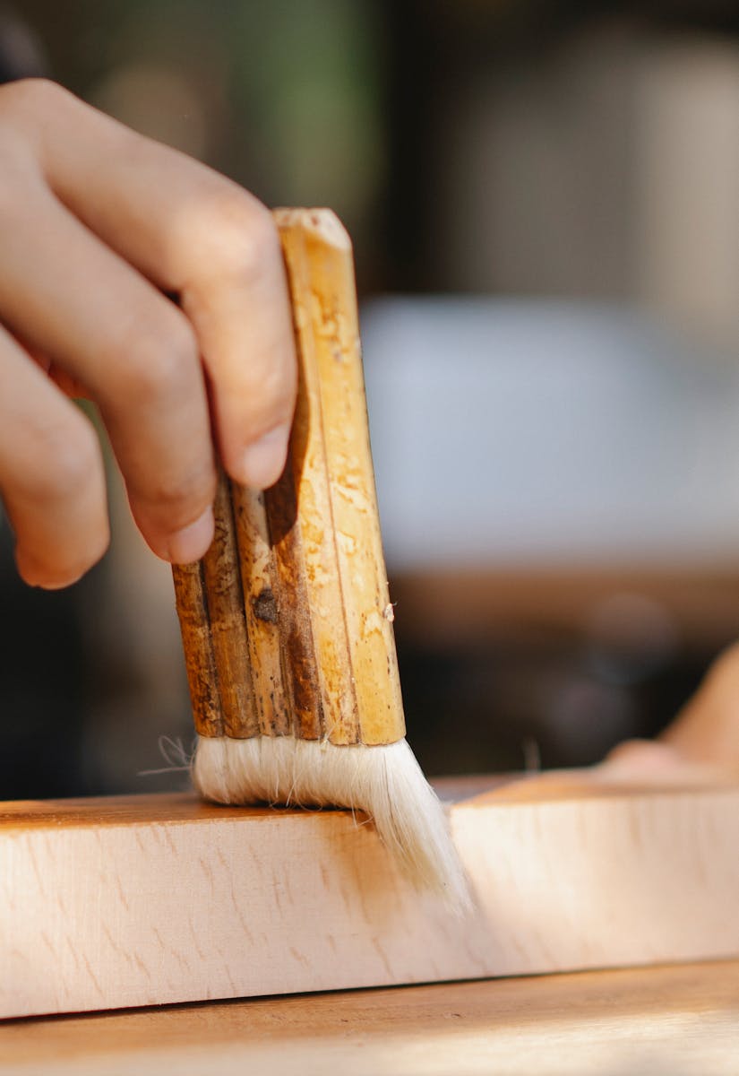 Unrecognizable craftsman applying glue on wooden board while working in joinery on blurred background